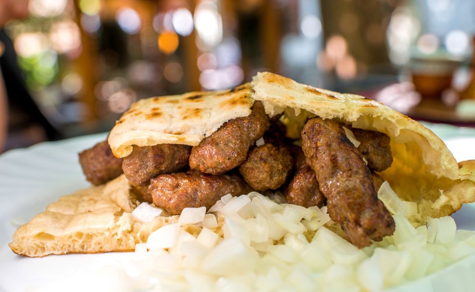 Bun with cevapi and fresh onions served on a plate 